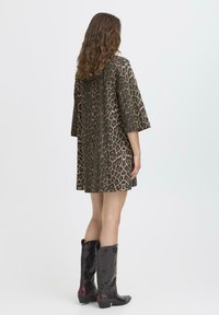 Oversized Kleid mit Leopardenmuster in Brauntönen und weiten Ärmeln, kombiniert mit knielangen schwarzen Leder-Stiefeln im Cowboy-Stil mit geprägten Details.