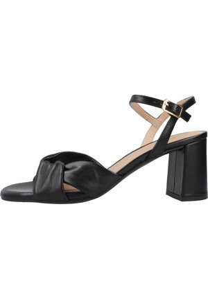 Sandaletto con tacco da donna in pelle nera, con cinturino frontale intrecciato, cinturino regolabile alla caviglia con fibbia dorata e tacco a blocco su sfondo bianco.