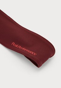 Burgundy fabric headband with stitching details, featuring "Peak Performance" logo in red. Smooth texture, curved shape, and flexible design.