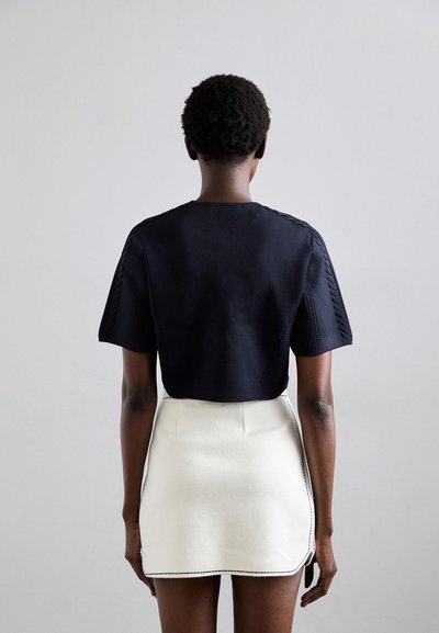 Top corto blu navy con maniche texturizzate, abbinato a una gonna bianca con orlo ricamato e dettaglio con tasche laterali.