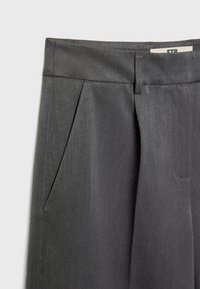 Pantalon gris foncé sur mesure avec plis avant, poches latérales et passants de ceinture visibles sur un fond uni.