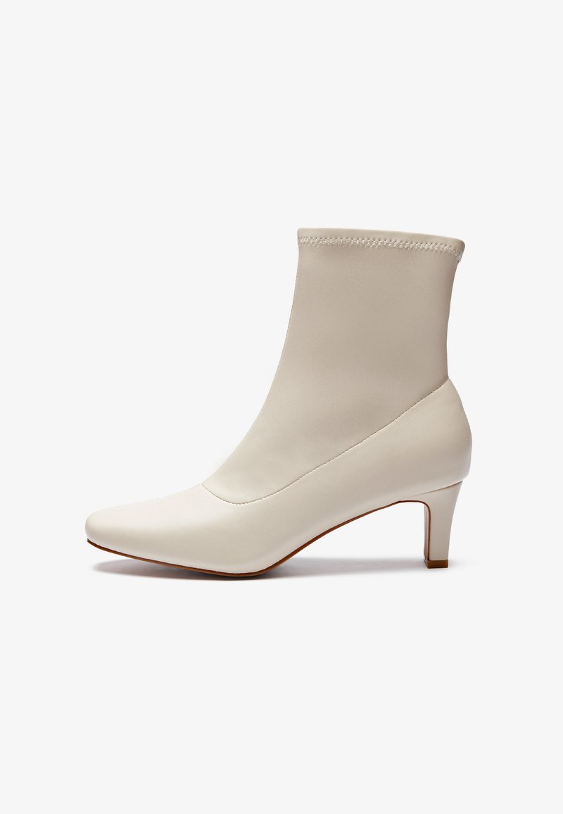 Botín blanco hasta el tobillo hecho de cuero suave con punta afilada y un tacón corto y cónico. Presenta un diseño minimalista y un empeine sin costuras.