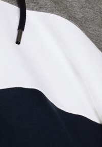 Tissu à blocs de couleurs avec des sections grises, blanches et bleu foncé, et un cordon noir avec une pointe en métal.