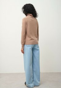 Beige polotröja i mjukt material, kombinerad med ljusblå vida jeans. Slimmad passform vid midjan och avslappnad silhuett vid benen.