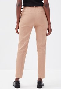 Pantalons beiges en tissu lisse, dotés d'une coupe ajustée, de poches latérales et de poches arrière, terminés par une taille cintrée.