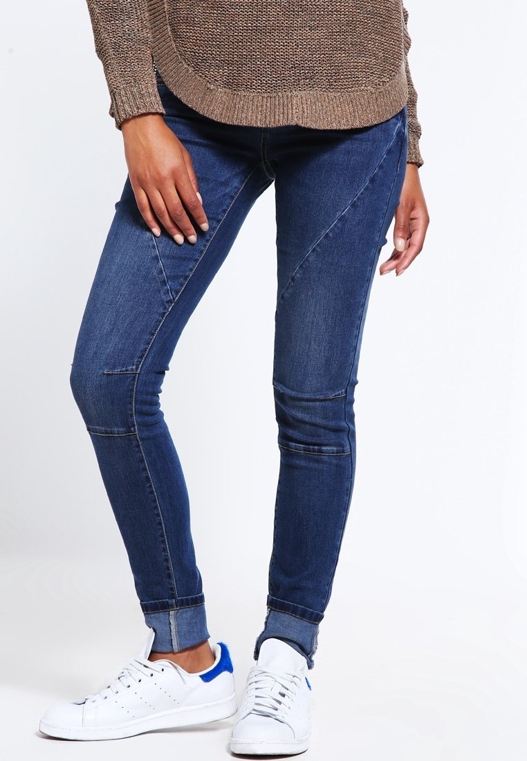 Jeans skinny azul oscuro con costuras de panel en contraste, con una cintura de altura media y bajos remangados. Combinados con zapatillas blancas.