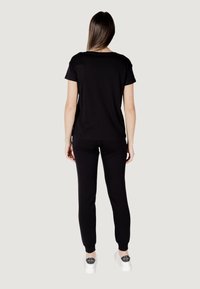 T-shirt nera a maniche corte e pantaloni neri, entrambi in un tessuto morbido. Abbinati a sneakers bianche con un accento nero sul tallone.