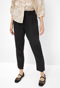 Zwarte, loszittende broek met een textuurafwerking en een elastische tailleband, gedragen met zwarte mesh flats, boven een licht gestippeld topje.