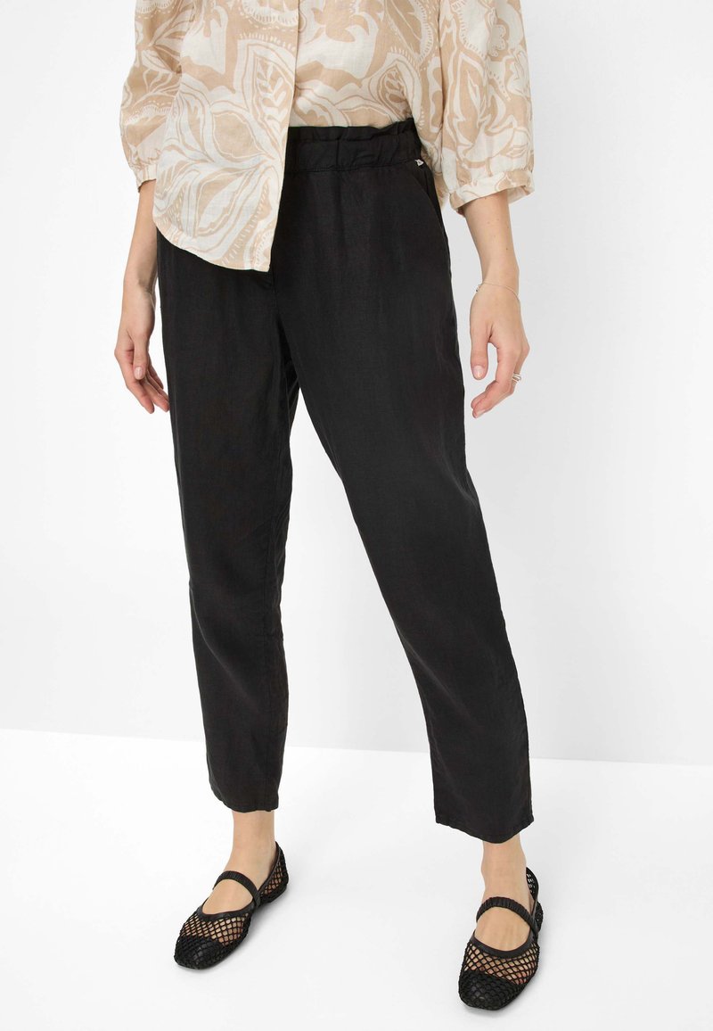 Zwarte, loszittende broek met een textuurafwerking en een elastische tailleband, gedragen met zwarte mesh flats, boven een licht gestippeld topje.