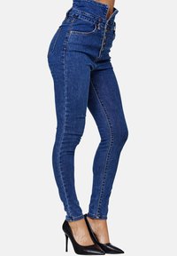 Jeans de denim azul de cintura alta y ajuste slim, con cierre de cinco botones, costuras en contraste y una textura suave.