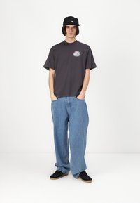 Grå t-skjorte med et sirkulært grafisk design, løse lys blå jeans og svarte joggesko. Bært med en svart caps, minimalistisk design.