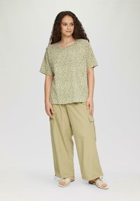 Zielona bluzka w kropki z okrągłym dekoltem, zestawiona z lekkimi khaki spodniami cargo z bocznymi kieszeniami i ściągaczami na mankietach.