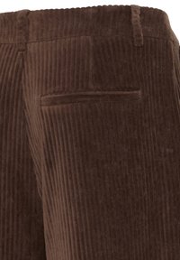 Pantalon en velours côtelé marron en gros plan montrant la poche passepoilée arrière et les passants de ceinture avec une texture côtelée verticale.