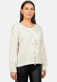 Maglione bianco a maglia con motivo a stampa leopardata, scollo a V con dettaglio a fiocco, e polsini e bordo a costine. Abbinato a pantaloni neri.