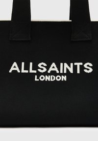 Sac cabas en tissu noir avec deux anses et l'inscription "ALLSAINTS LONDON" en lettres majuscules blanches au centre devant.
