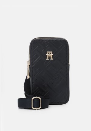 Pochette pour téléphone zippée noire en cuir texturé, avec un motif géométrique et un accent de logo doré. Inclut une bandoulière amovible.