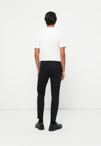 Zwarte slim-fit broeken van gladde stof, met een subtiele glans, achterzakken en gedragen met zwarte schoenen en een wit shirt.