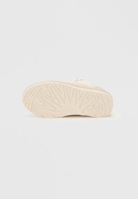 Suola di scarpa in gomma beige con un motivo di presa testurizzato, caratterizzata da un logo circolare. Superficie liscia con bordi arrotondati e dettagli minimi.