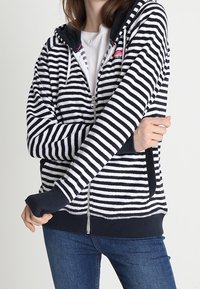 Gestreepte capuchontrui met rits in marineblauw en wit. Voorzien van een capuchon met trekkoord, zakken aan de voorkant en geribbelde manchetten. Zachte stof met een gestructureerde afwerking.
