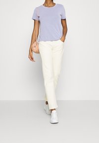 Ljuslila t-shirt med kort ärm i kombination med krämfärgade, strukturerade raka byxor och vita sneakers, bärande en liten rosa v äska.