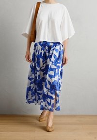 Un haut blanc à manches courtes associé à une jupe à motif floral bleu. La jupe présente une fente haute, et le modèle porte des chaussures tressées beiges.