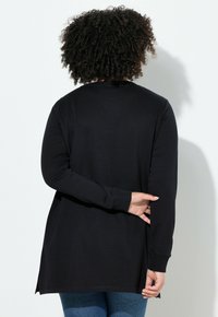 Top nero a maniche lunghe con orlo arrotondato, texture morbida e fessure laterali per un facile movimento. Presenta una vestibilità ampia e un collo a giro.