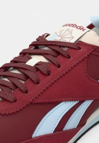 Rdeča atletska superga iz semiša in sintetičnih materialov, z modrimi akcenti, teksturiranimi vezalkami in blagovno oznako na jeziku.