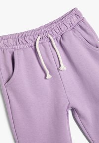 Pantalones de chándal morados con cintura elástica, cordón y dos bolsillos laterales. Tejido suave con una textura lisa.