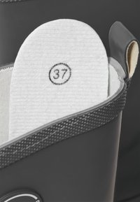 Valge jalanõu tallakate suurusega 37, mis on trükitud ringi kujul, sisestatud tumehallidesse saapasse, mille ülemine ääris on tekstureeritud.