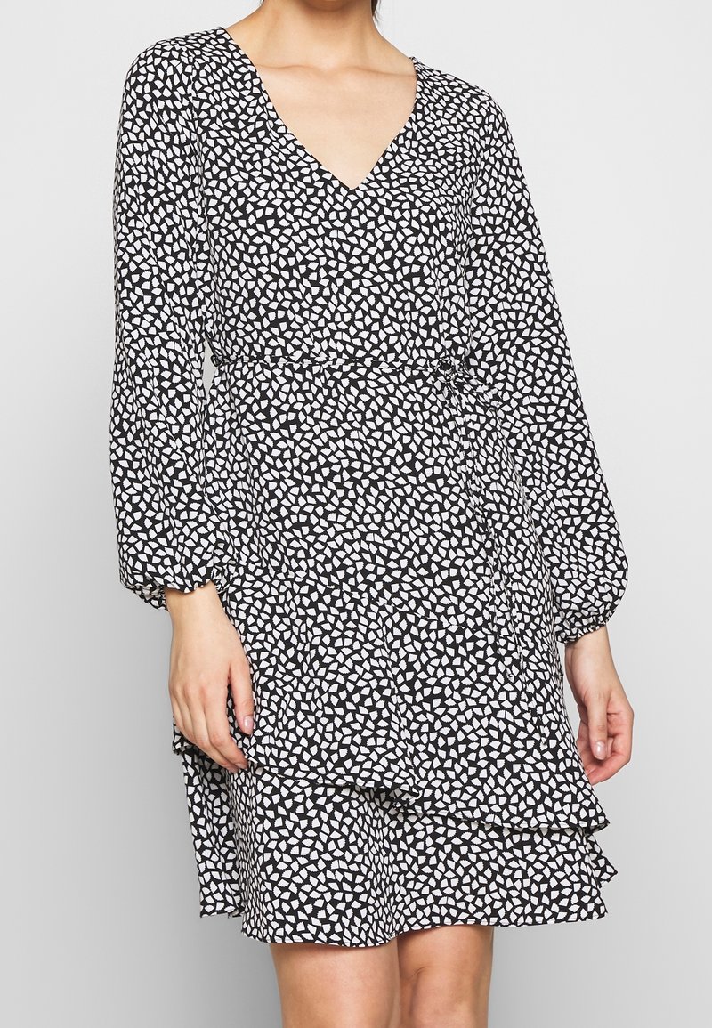 Black dress with a V-neck and long sleeves, featuring a white abstract pattern. The hem includes a ruffled detail and an adjustable waist tie.