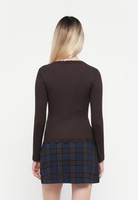 Brun langermet topp med ribbet tekstur og bølget kant, kombinert med et blått og brunt rutete skjørt med rett snitt.
