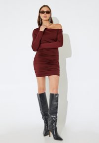 Burgunderfarbenes, schulterfreies Kleid mit geraffter Textur und figurbetontem Design. Kombiniert mit knielangen, schwarzen Stiletto-Stiefeln im Krokodil-Print.