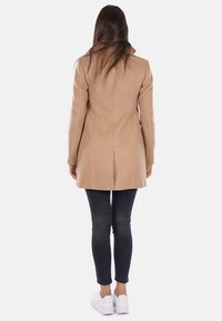 Cappotto in misto lana beige con vestibilità su misura, maniche lunghe e design di lunghezza intermedia. Abbinato a jeans skinny scuri e sneakers bianche.
