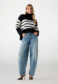 Maglione a righe bianche e nere, stile dolcevita, abbinato a jeans a vita alta larghi di colore azzurro chiaro e tacchi a spillo neri.