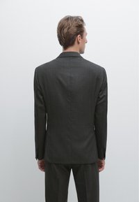 Giacca da abito su misura grigio scuro con silhouette strutturata, rever a lancia e spacco posteriore doppio. Tessuto liscio con dettagli sottili di texture.