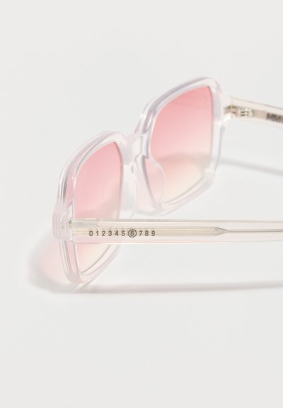 Διαφανή γυαλιά ηλίου με φακούς σε ροζ διαβάθμιση, τοποθετημένα σε λευκή επιφάνεια, με αριθμητική λεπτομέρεια στο πλαίσιο.