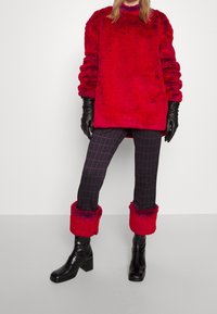 Un pull surdimensionné en fausse fourrure rouge avec des poignets côtelés, associé à un pantalon à carreaux noir et rouge et des bottes noires jusqu'aux genoux avec des talons épais.