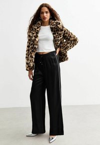 Giacca in pelliccia sintetica con stampa leopardo, top corto bianco, pantaloni neri a gamba larga in satin con strisce laterali e décolleté metalliche a punta.