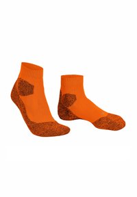 Un paio di calzini alla caviglia arancioni con tallone, punta e zone di supporto dell'arco rinforzati e di colore scuro su uno sfondo bianco.