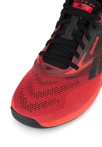 Punase ja musta värvusega Reebok Nano XV jalanõu, mille ülaosa on tekstuuriga ja kootud, varustatud musta paeltesüsteemi ja voolujoonelise, struktureeritud varbakaitsega.