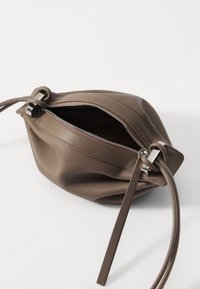 Brown leather bag with a soft, rounded shape. Features a top zipper with silver hardware and a thin, matching strap. Interior is dark.