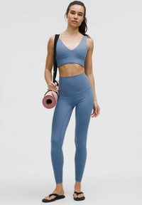 Kék sportmelltartó és magas derekú leggings rugalmas anyagból. Az öltözet sima textúrájú és minimális varrásokkal rendelkezik. Egy jóga mat és táska is tartozik hozzá.