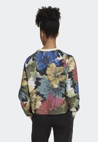 Sweatshirt à motif floral mettant en avant un mélange de fleurs bleues, roses, jaunes et vertes, avec un col rond et des poignets côtelés.