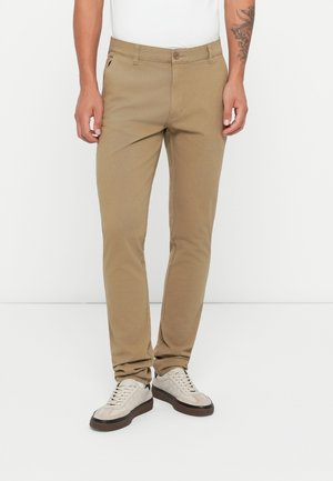 Khaki pants made of cotton blend, featuring standard fit, two side pockets, and button closure. Paired with light-colored sneakers.