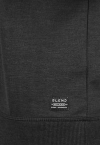 Felpa nera con un tessuto testurizzato, orlo a coste e un'etichetta con il marchio "BLEND" e il testo "GLOBAL JEANMAKER".