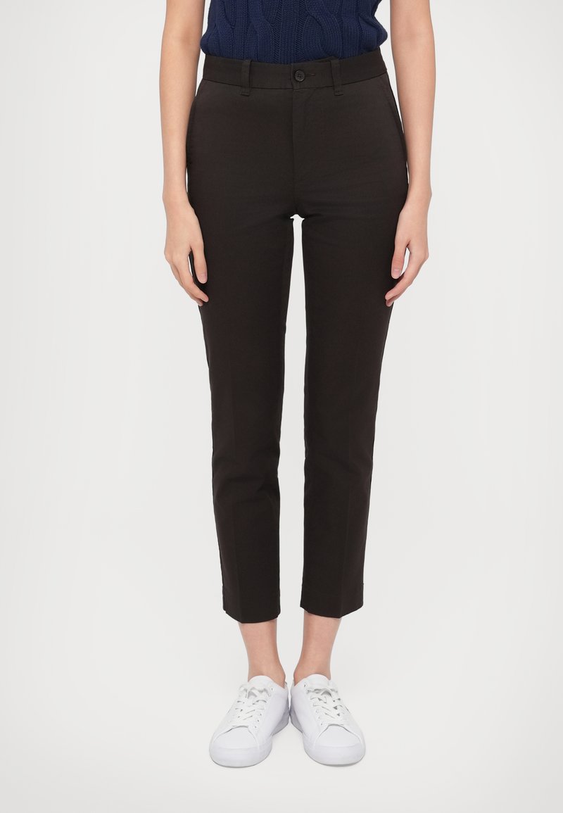 Μαύρο, εφαρμοστό παντελόνι με κούμπωμα κουμπιού, μέχρι τον αστράγαλο, με λεία υφή, φορεμένο με λευκά αθλητικά παπούτσια.