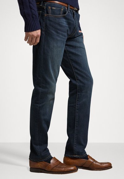 I jeans in denim blu scuro presentano un design a gamba dritta, tasche anteriori e dettagli di cucitura sottili. Abbinati a mocassini in pelle marrone.