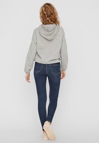 Sudadera gris con capucha, combinada con jeans ajustados de color azul oscuro. El conjunto incluye zapatos beige sin cordones y presenta un ajuste relajado y una textura suave.