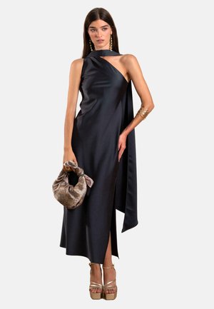 Schwarzes Satin-Kleid mit asymmetrischem Ausschnitt, seitlichem Schlitz und drapiertem Detail. Kombiniert mit einer strukturierten goldenen Clutch und Riemchen-Plateau-Pumps.