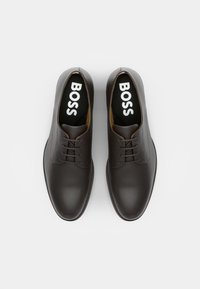 Scarpe eleganti in pelle marrone con finitura liscia, design con lacci, punta rotonda e soletti neri con il logo "BOSS" stampato in bianco.